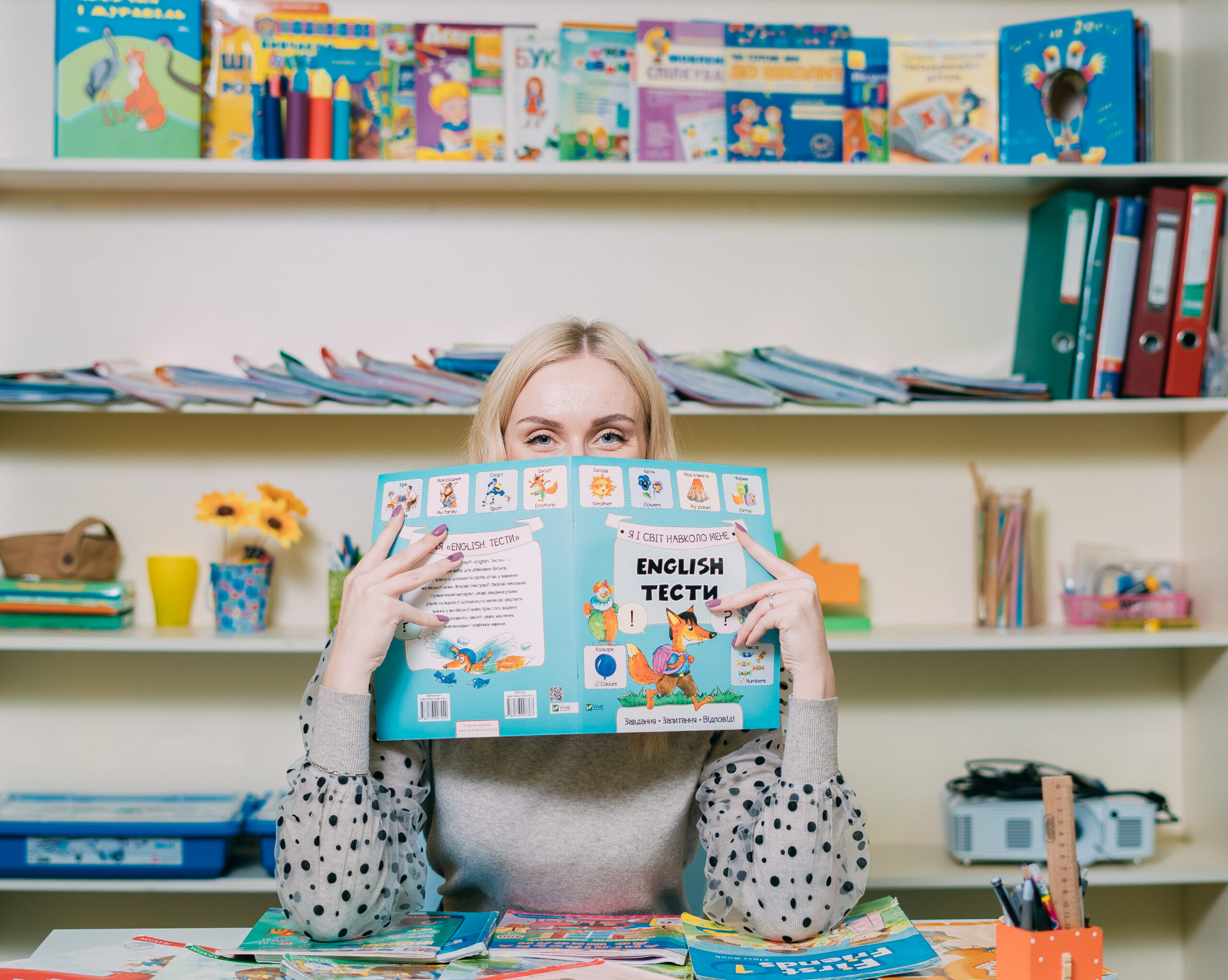 Woman reading an English book in a colorful classroom setting.